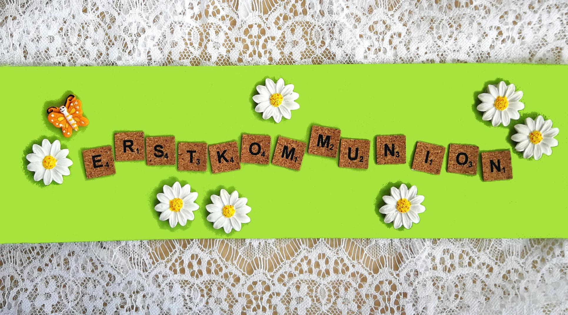 Erstkommunion Holzbuchstaben „Erstkommunion“ auf grünem Hintergrund, umgeben von Gänseblümchen und Schmetterling.